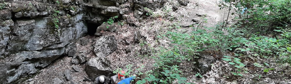 View of an approximately 15' deep sinkhole with a student entering a cave.