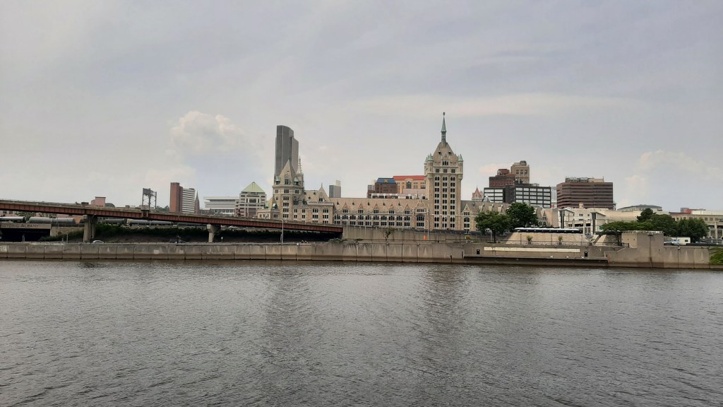 River in foreground, with the old D&H building in the midground and Corning Tower left of center in the background.
