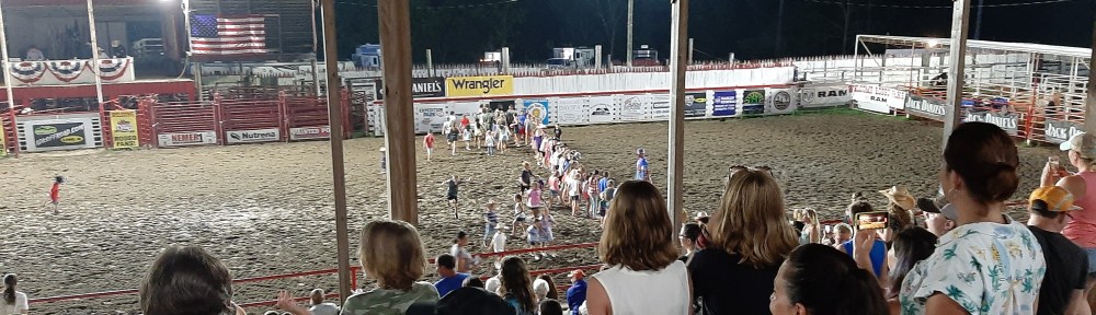 Shot from bleachers looking at a rodeo arena with kids lined up for a race.