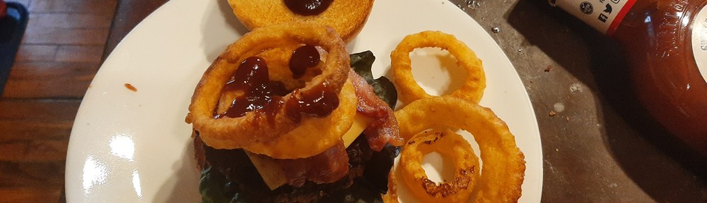 BBQ burger with 2 onion rings, some bacon and cheese on top.